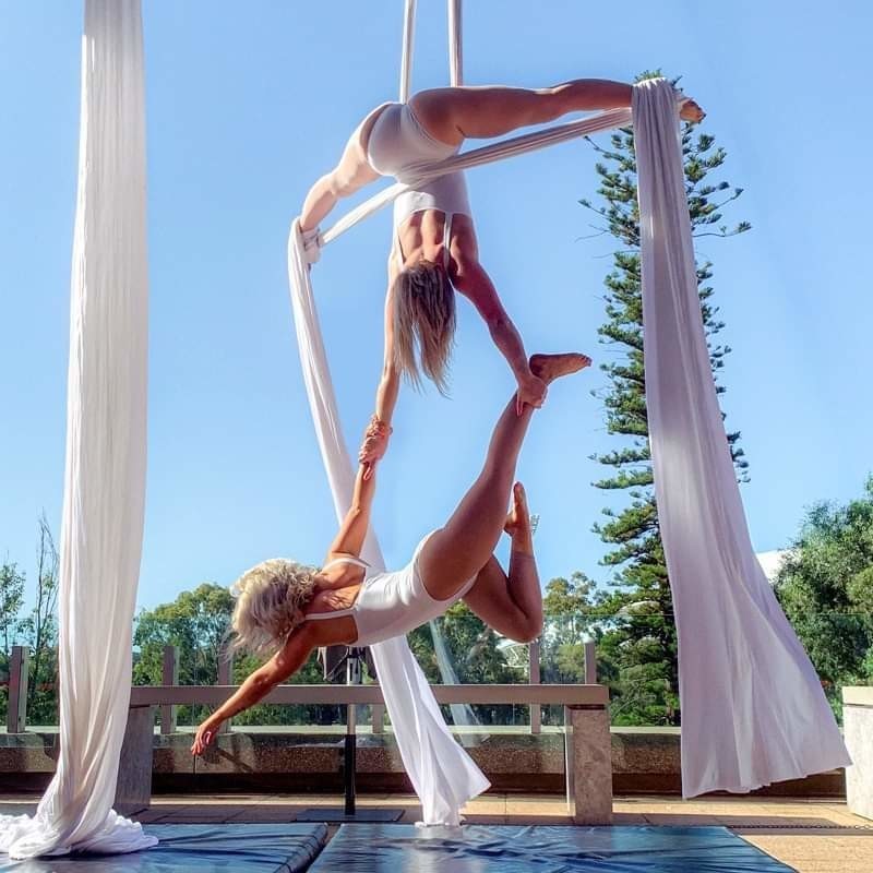 Aerialicious - Two performers wearing all white are hanging in white skilks updside down and outside.