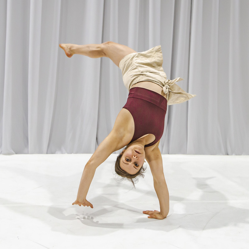 A girl doing an acrobatic trick balancing on one hand while looking at the camera with a concentrated expression on her face