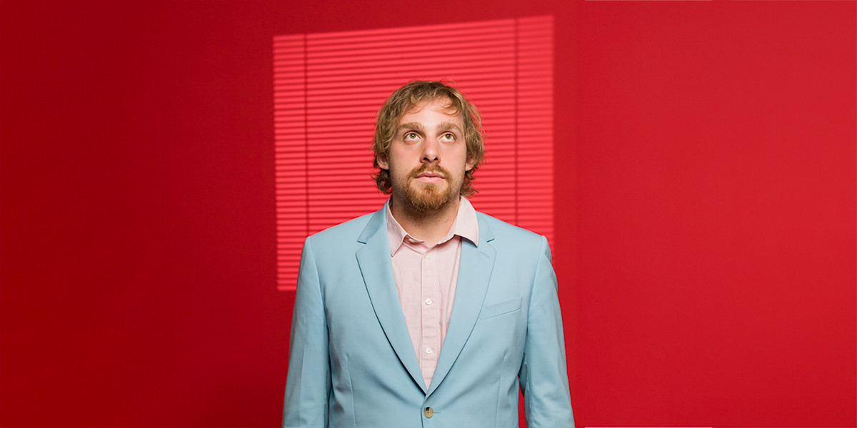 Jacob Henegan in a light blue suit against a red background