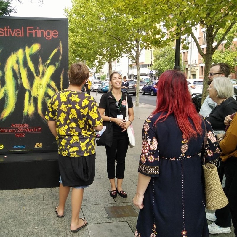 A guide shows her guests an Adelaide Fringe poster on the Adelaide Fringe: A History walking tour.