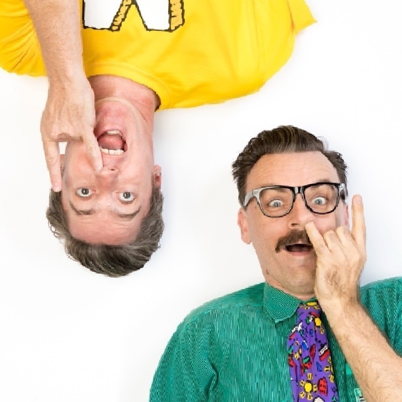 An image of two men (Matt and Rich) with their little fingers in their noses. Richard has glasses and a green shirt with colourful tie. Matt is wearing a yellow shirt and is upsidedown.