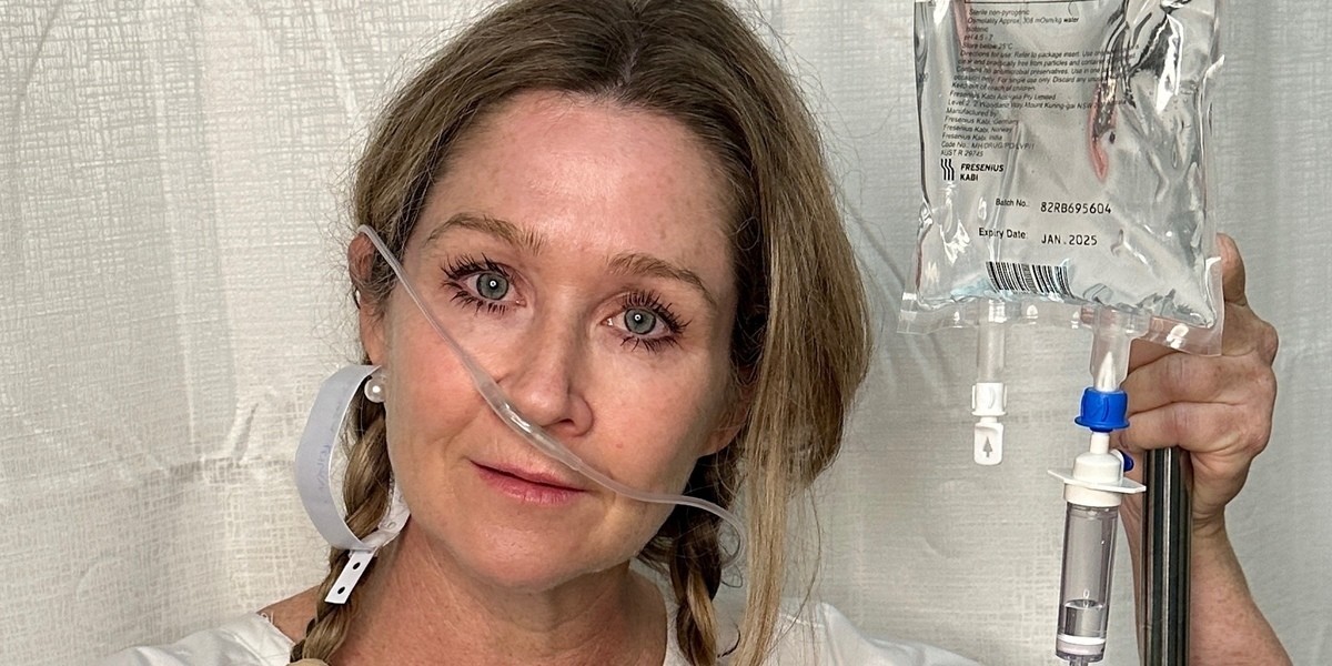 Between the Curtains - A women is standing and staring with a nasal oxygen tube falling from her left nostril.  She has a hospital ID band as an earring, she is holding a green bedpan in her right arm and her left hand is holding an IV stand with a saline bag attached.
