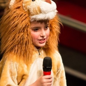 Picture of girl dressed as a lion singing into a microphone.