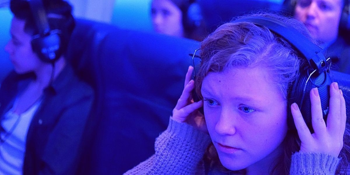 A girl is sitting in the purple-lit flight container, looking slightly nervous as she places her headphones on her head.