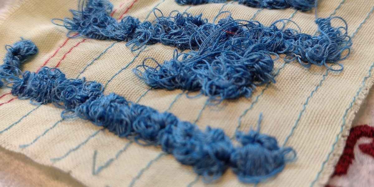 Lots of fluffy blue threads are visible on a fabric square stitched to look like a Post It note.