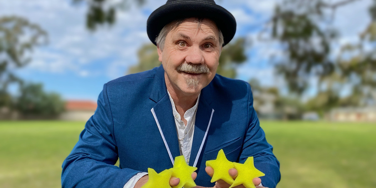 Drew Magic, the star of our show, wearing a blue suit and black hat, holding 4 yellow stars.