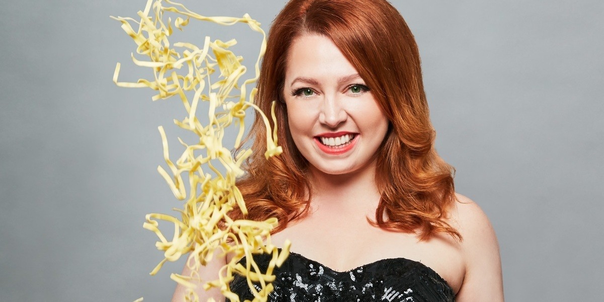 Comfort Food Cabaret - Woman in black sequin dress with red hair tossing pasta in the air