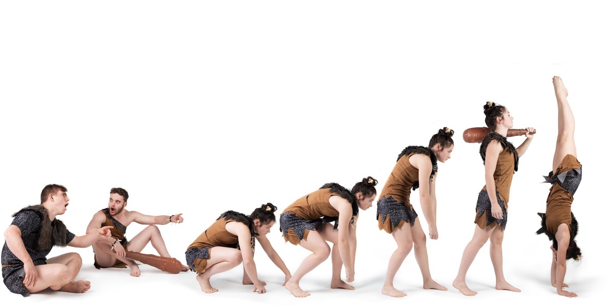 A series of different positions of cave person, showing the evolution of a cave woman from knuckle dragging through to standing, ending in an acrobatic handstand.