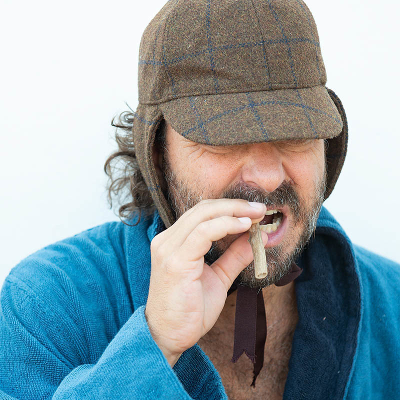DR. BROWN BETURNS - A hairy man in a blue dressing gown is chewing on a stick. He looks like he has wandered out from the mountains. He is wearing a tartan detectives hat.