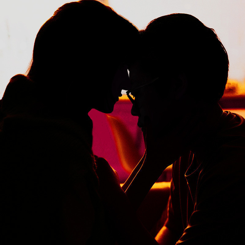 Good Talk - Streaming From Sydney - The silhouettes of two people touching foreheads in affectionate manner. The background is blurry pink and orange  furniture.