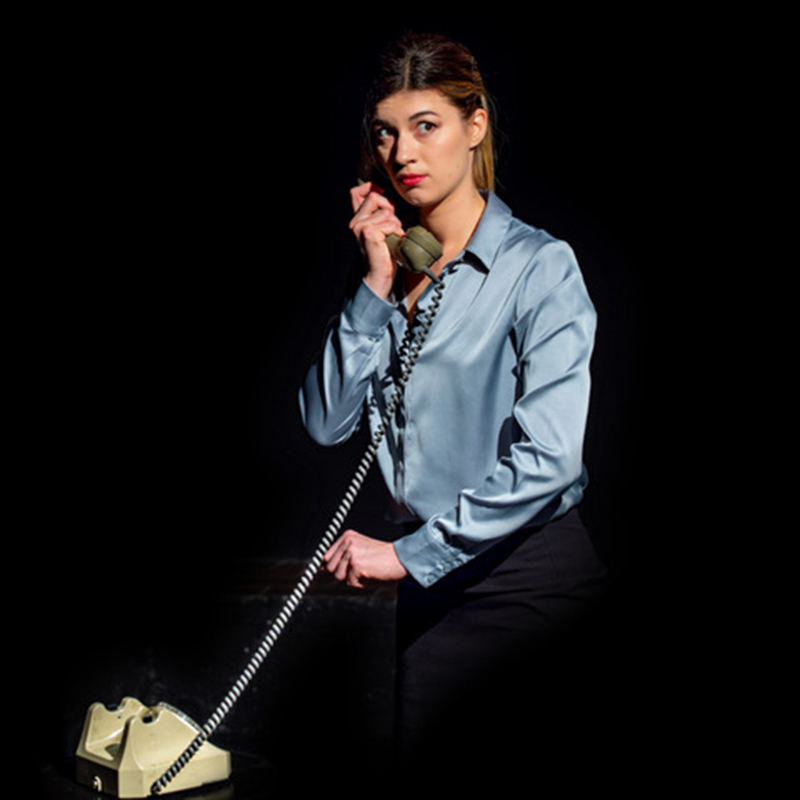 Woman in a blue blouse looking at you talking on a telephone.
