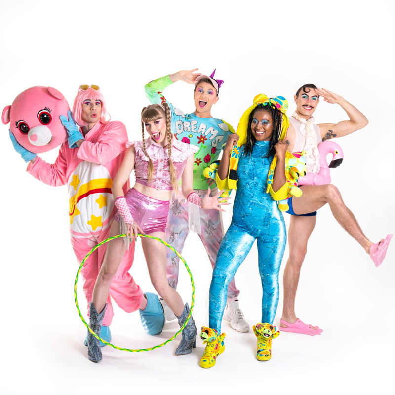 Five performers wearing colourful and bright costumes pose as a group.
