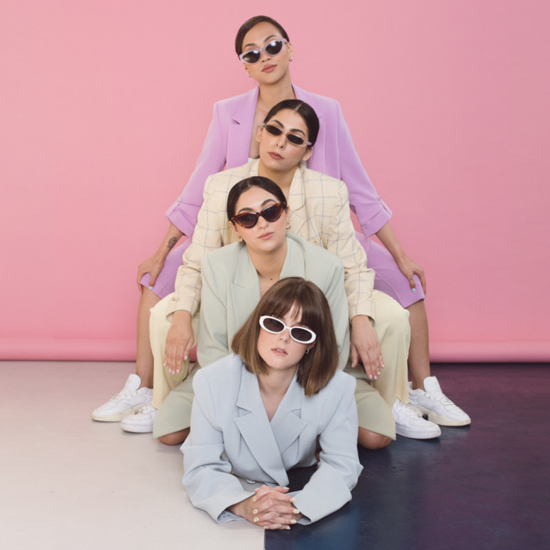 The Cherry Poppers - Four females in coloured suits wearing sunglasses stacked on top of one another.