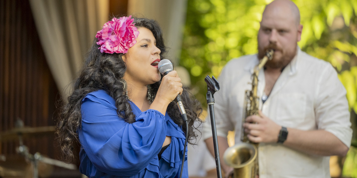A lady in blue dress holding a microphone while singing to guy playing a sax