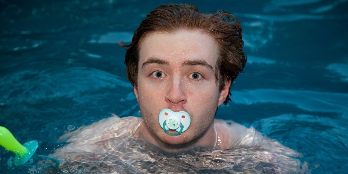 A closeup of a grown man swimming in a pool with a dummy in his mouth.