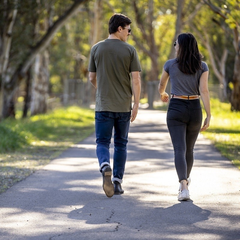 Two people walking along a path on a sunny day surrounded by nature.