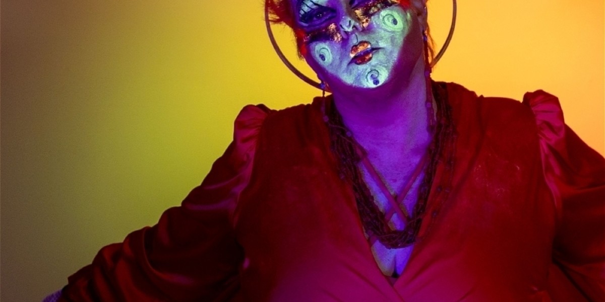 Madam Nightingale (Phaedra Gunn) dancing in red costume & headdress with UV stage makeup