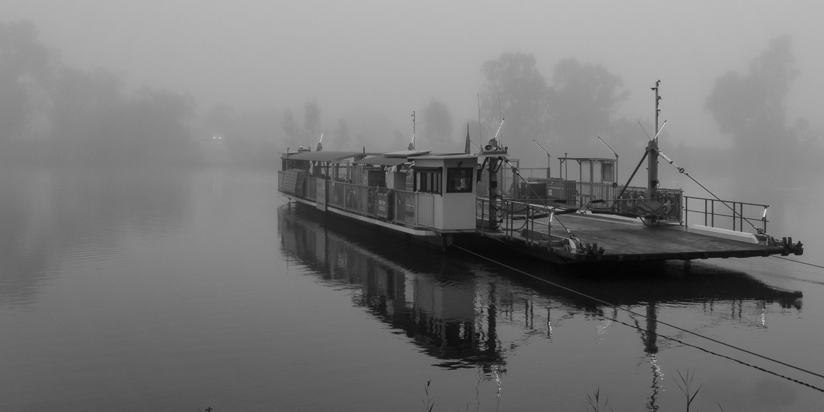 Waikerie ferry on a still wintery morning reflected in the water and surrounded by fog.