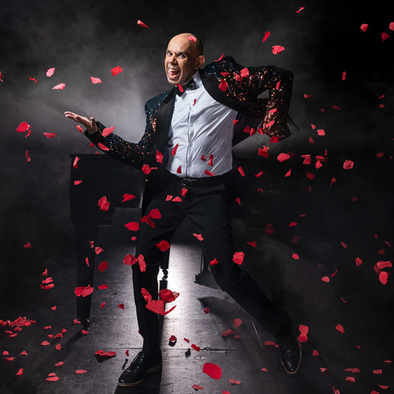 Comedian Steven Oliver is dancing and singing with a cheeky grin as rose petals descend on him