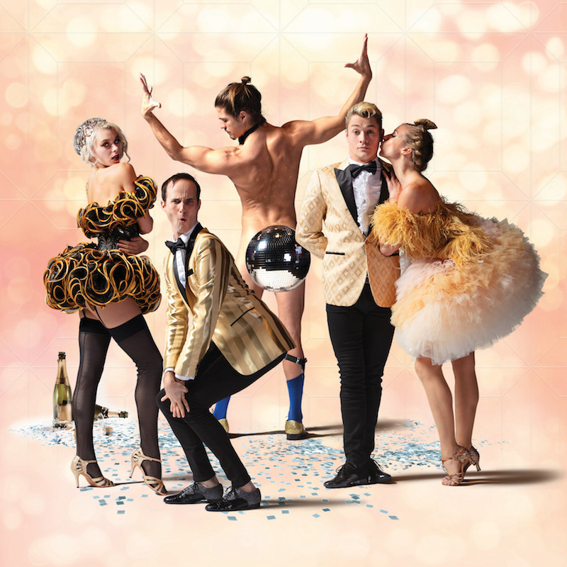 The cast of Blanc de Blanc Encore pose together in elaborate gold costumes on a sparkly peach background pulling faces that are cheeky, fun and engaging. There is confetti and a bottle of champagne at their feet.