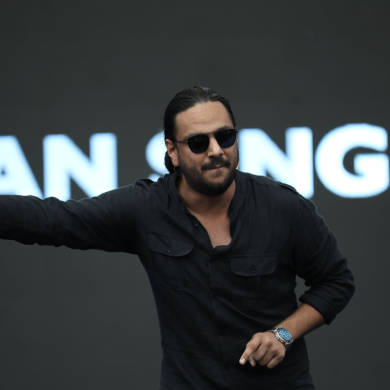 Performer, wearing a black shirt, sun glasses, on stage in the middle of his act, pointing to his right