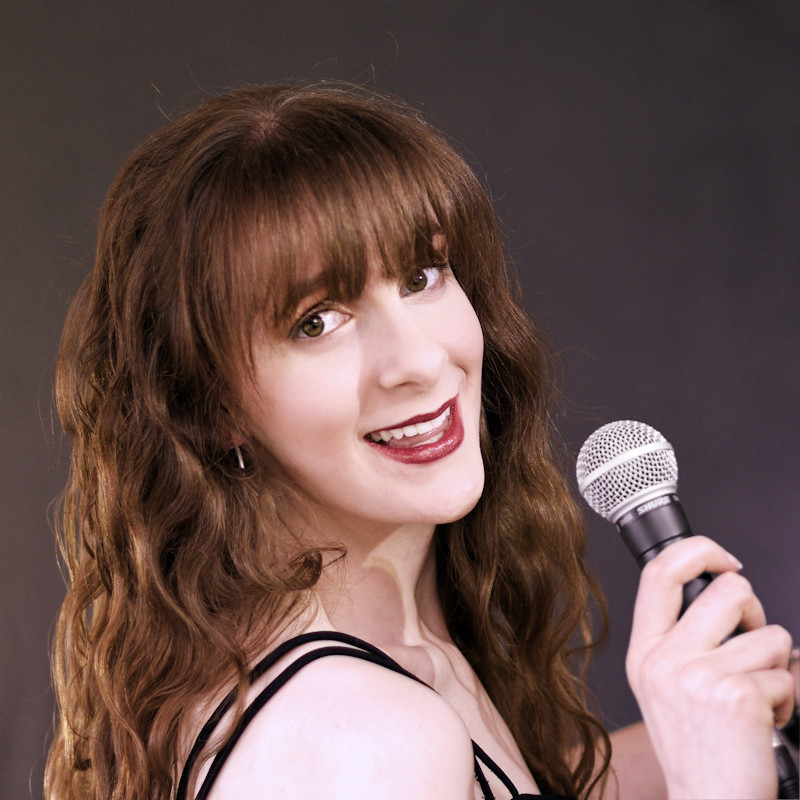 A performer (Tiffany Gaze) smiling invitingly and holding a microphone.
