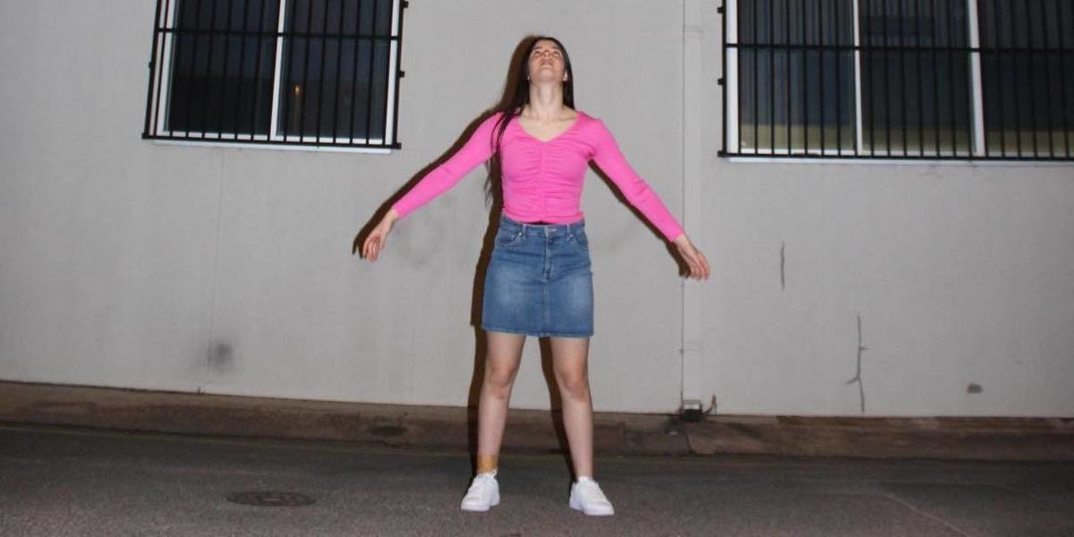 A girl stand outside at night looking up to the sky with arms outstretched.