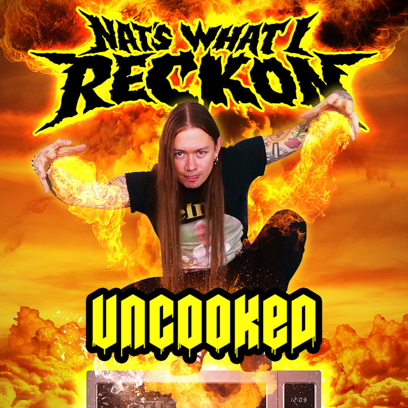 "Nat", a tattooed man with straight, long hair and facial piercings, stands against a fire background. Nat wears black jeans with a silver chain and a black T-shirt. He is standing with his hands outstretched.