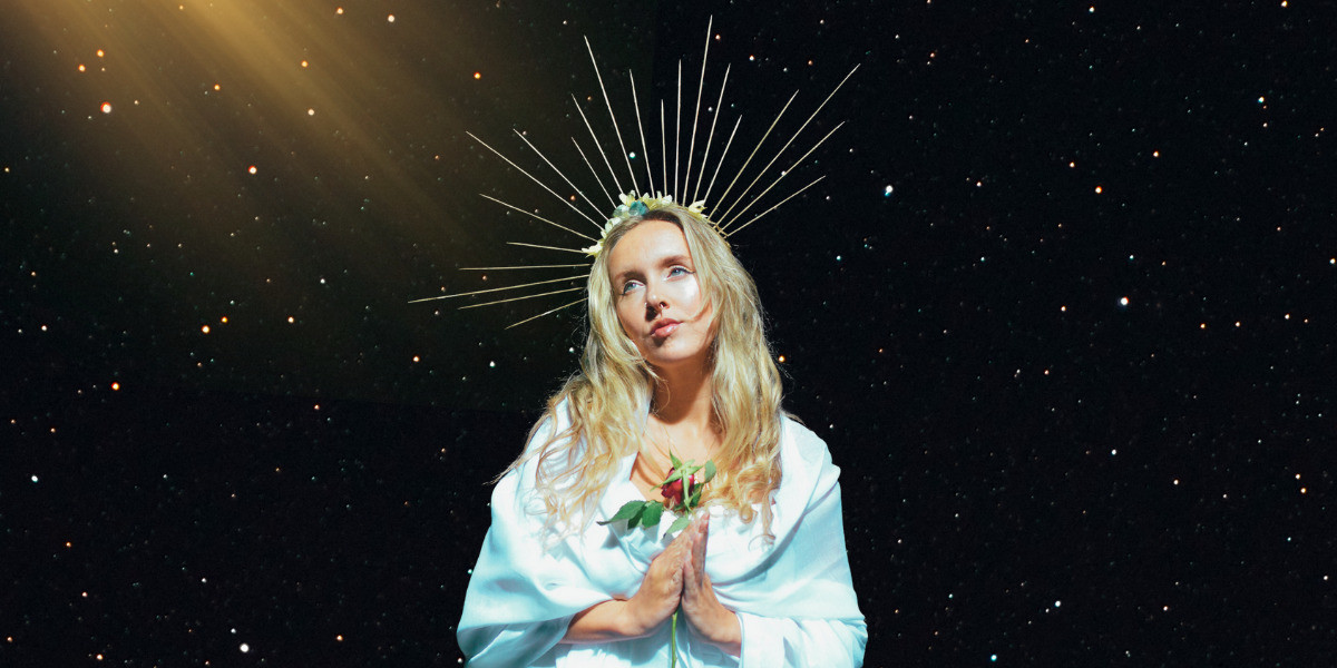 Dear God, please take me now - Image of actor dressed as Mother Mary over a cosmic, starry night background.