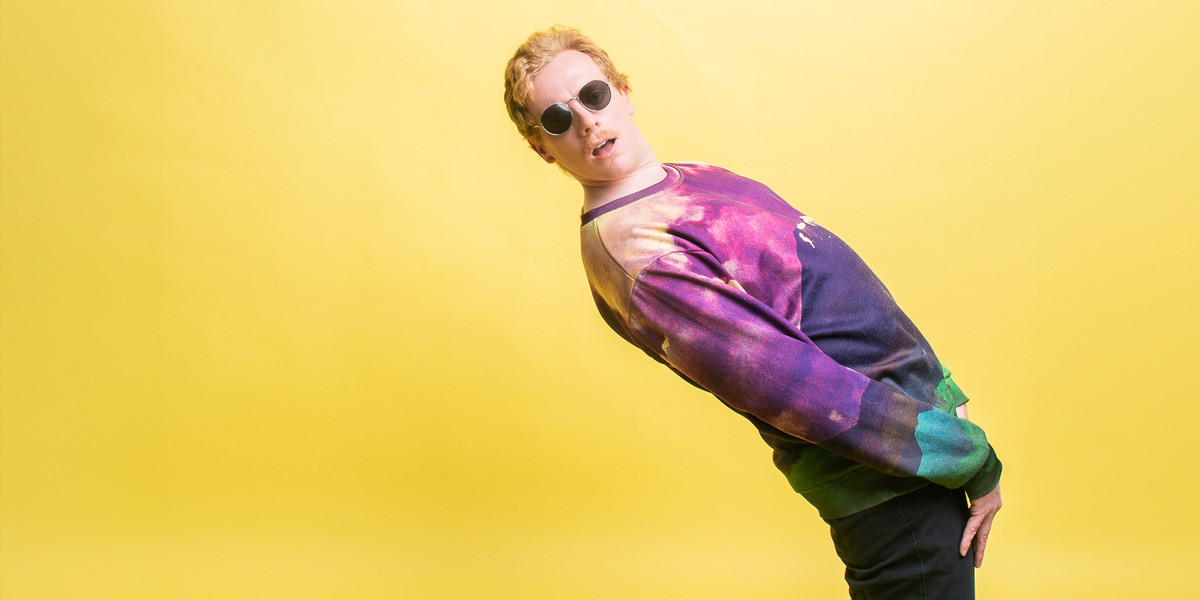Callum Straford: Mozart-182 - Callum is bending over backwards with remarkable flexibilty. He is wearing sunnies and a colourful jumper. The background is yellow.