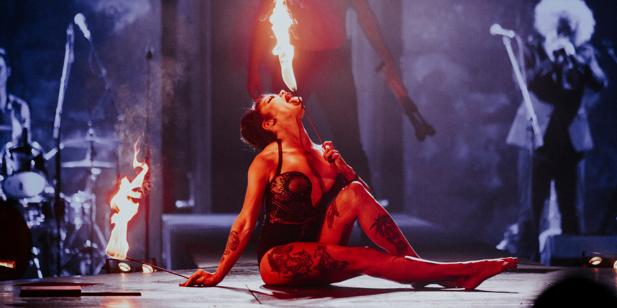 LIMBO - The Return performer sits on the stage for fire breathing stunt