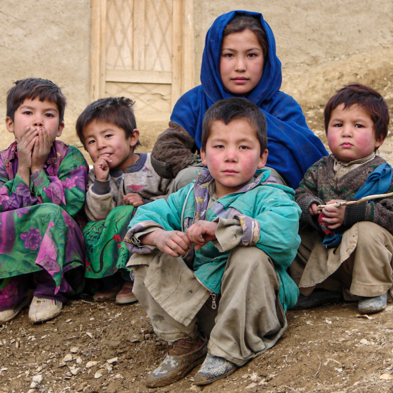 An Afghanistan Lost : Photography by Muzafar Ali - A Hazara woman and five children in bright and patchy clothing sit on the ground.