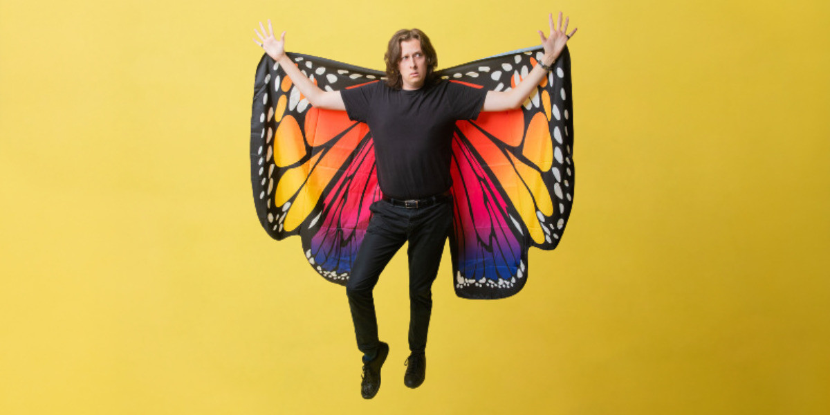Jon holding up butterfly wings. They are in front of a yellow background.