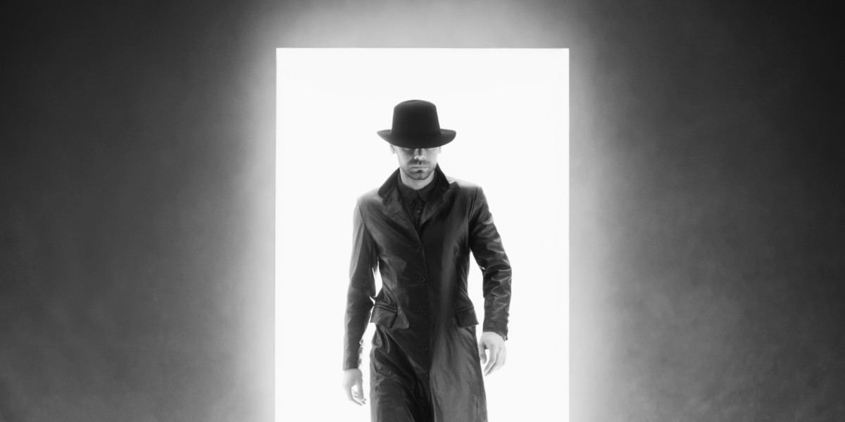 An Inspector Calls - With an air of intrigue, a sharply dressed man in a fedora stands before an open doorway, his silhouette casting a mysterious shadow into the room before him.