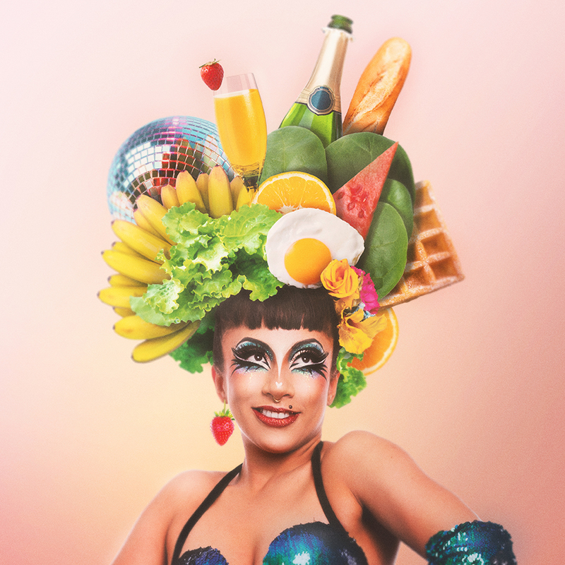 Jazida stands against a pink background wearing a headdress laden with breakfast food items and a disco ball.