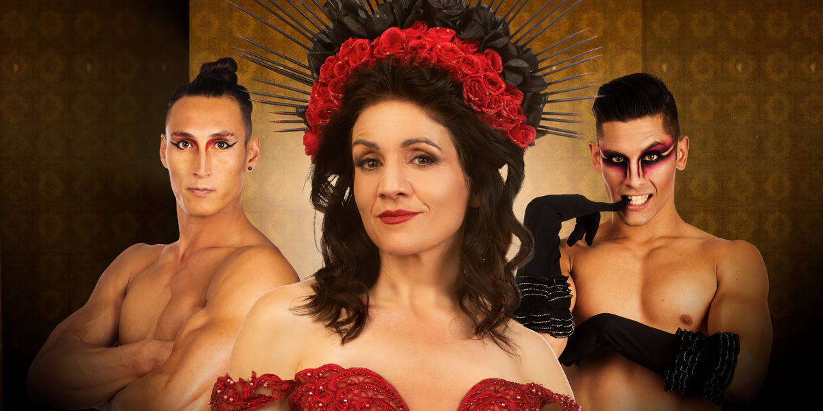 Rouge - Three people looking at the camera, head and shoulders visible. The woman in the centre is powerful, in a red spiked headdress and red dress, with a cheeky look on her face. On either side is a shirtless man, one with arms folded, a small amount of make up and muscles bulging. The other has a elaborate eye make up, a cheeky look on his face, and lacy gloves held up to his face.