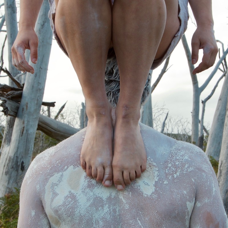 Cropped image, females feet on back of male who is covered in ochre.