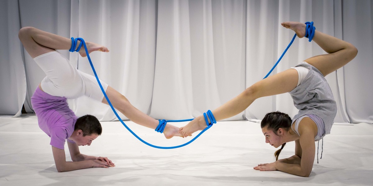 Two people in elbow stands with there back arched and their feet attached by blue ropes