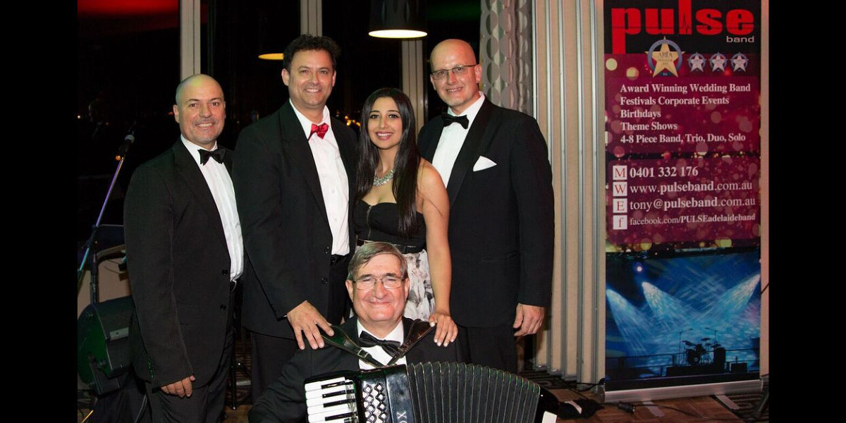This is an after concert photo. Standing up is Frank on the left with Tony standing along side him. In the middle is Sophia and Nige is on the right. Lino is kneeling down in the middle holding his piano accordion. Everyone is dressed in beautiful suits with bow ties.