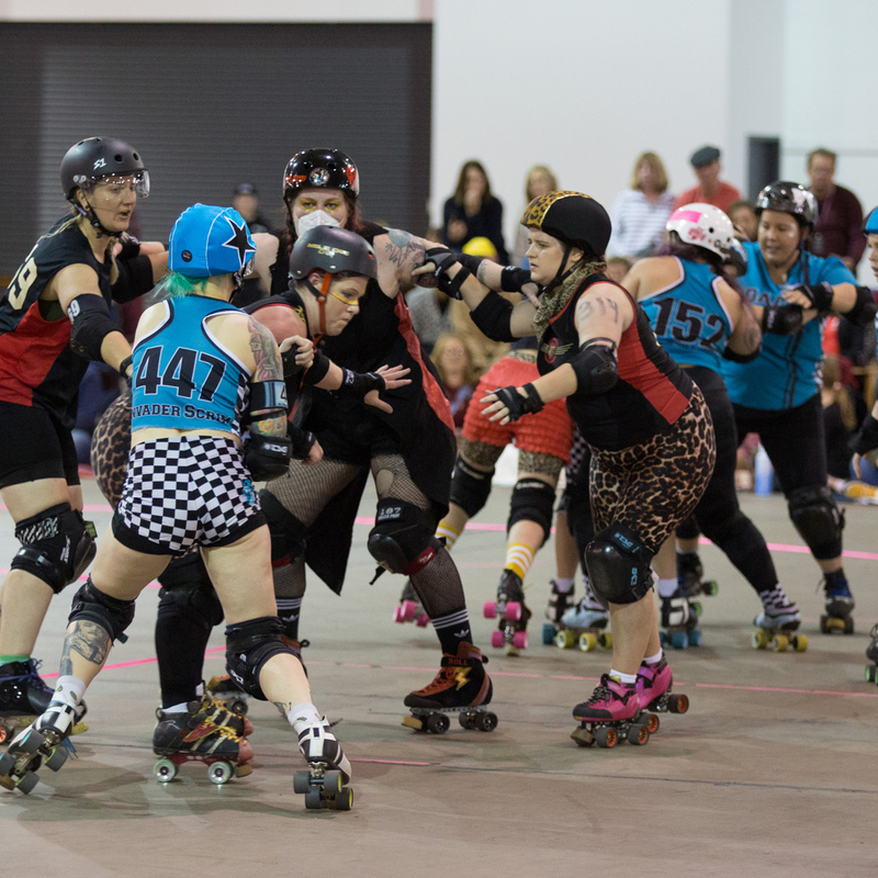 A roller derby game in action, with players being knocked by other players into the air or to the ground in a mess of limbs