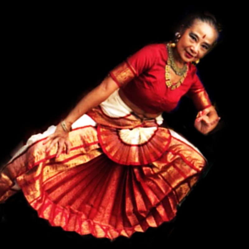 Indian dancer in white and red costume with one leg stretched forward.