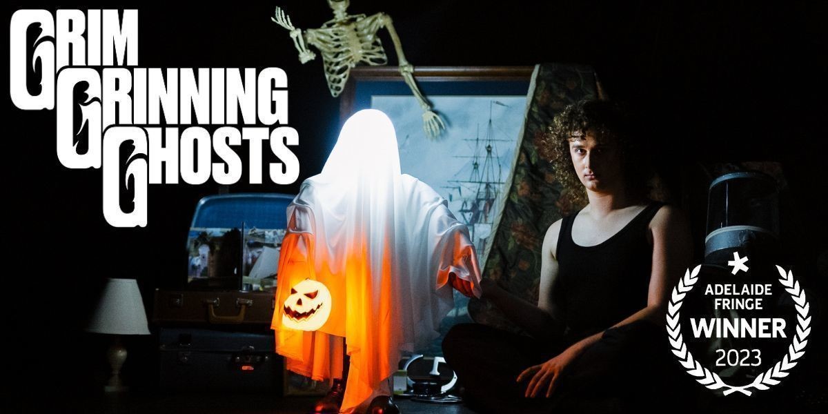 Grim Grinning Ghosts - Alix sits in front of props, including a skeleton, a picture frame, lamp and open suitcase. He holds the hand of an illuminated ghost, which is holding a pumpkin lantern. Alix has curly brown hair and stares intensely.