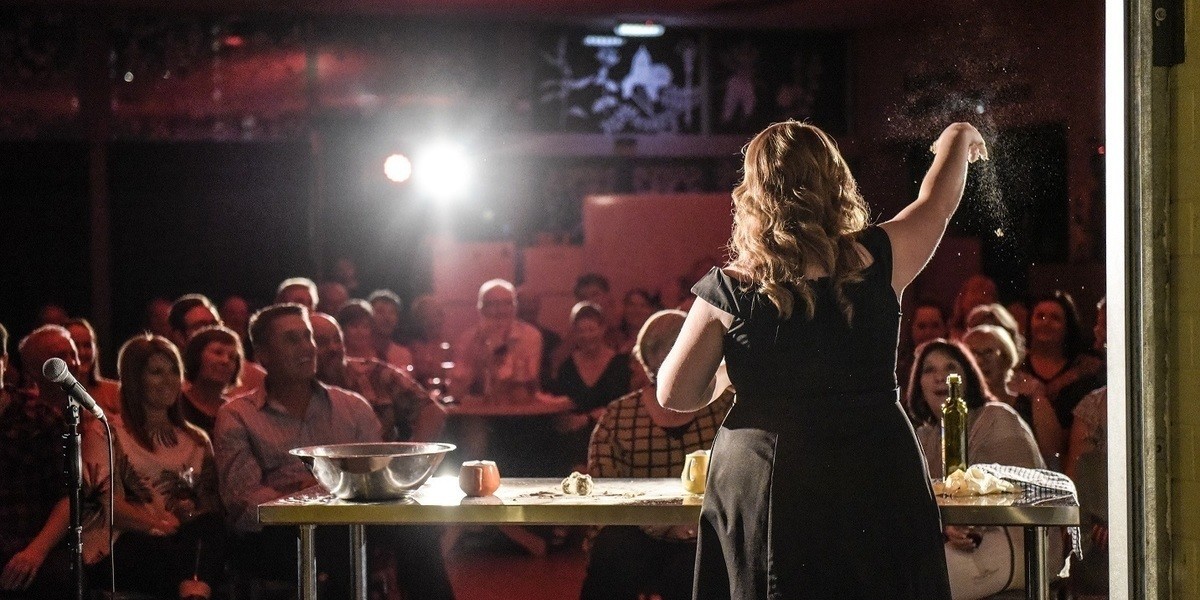 Woman in black dress cooking in front of a delighted audience