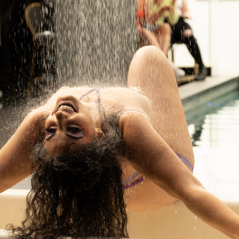 Performer leans over a performance bathtub with a shower raining down mid performance