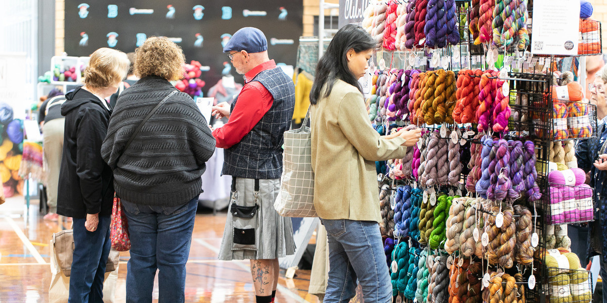 Folks admiring skeins of colourful yarn at a market