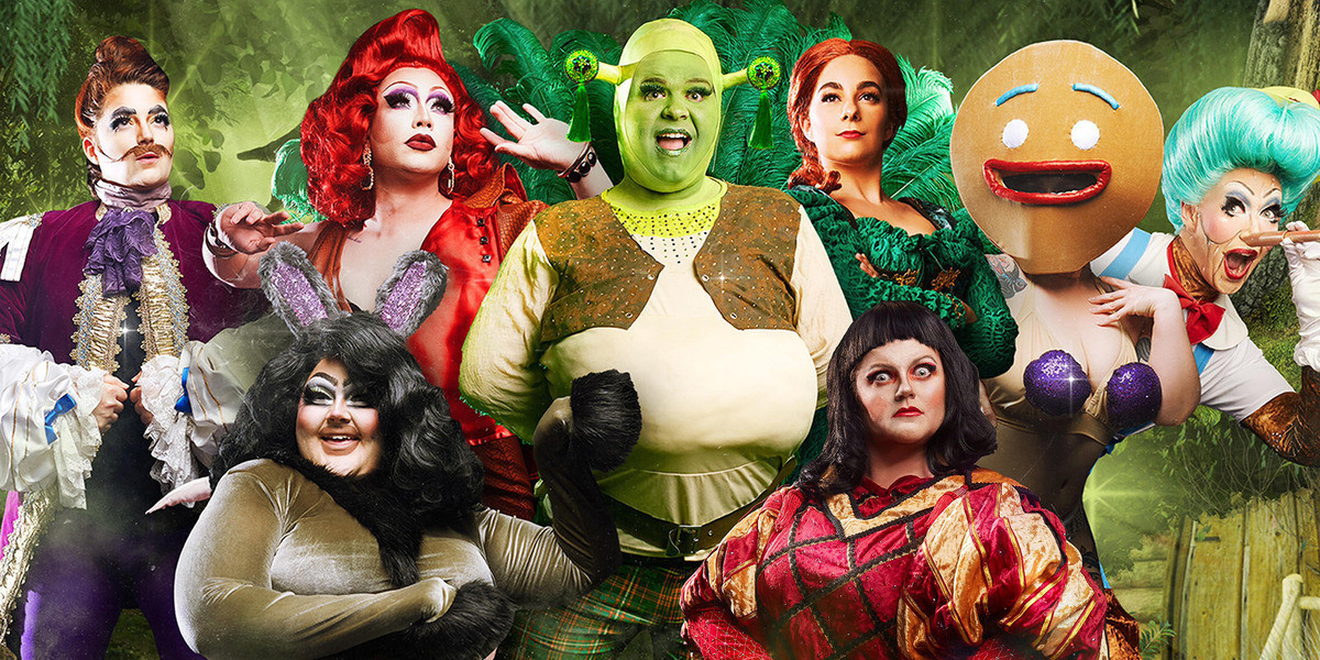 A group image of 8 performers dressed as characters from Swamplesque. L-R Magic Mirror in a purple suit, Donkey in a grey jumpsuit and large black wig. Dragon in a large red wig, Shrek in green facepaint and leather vest