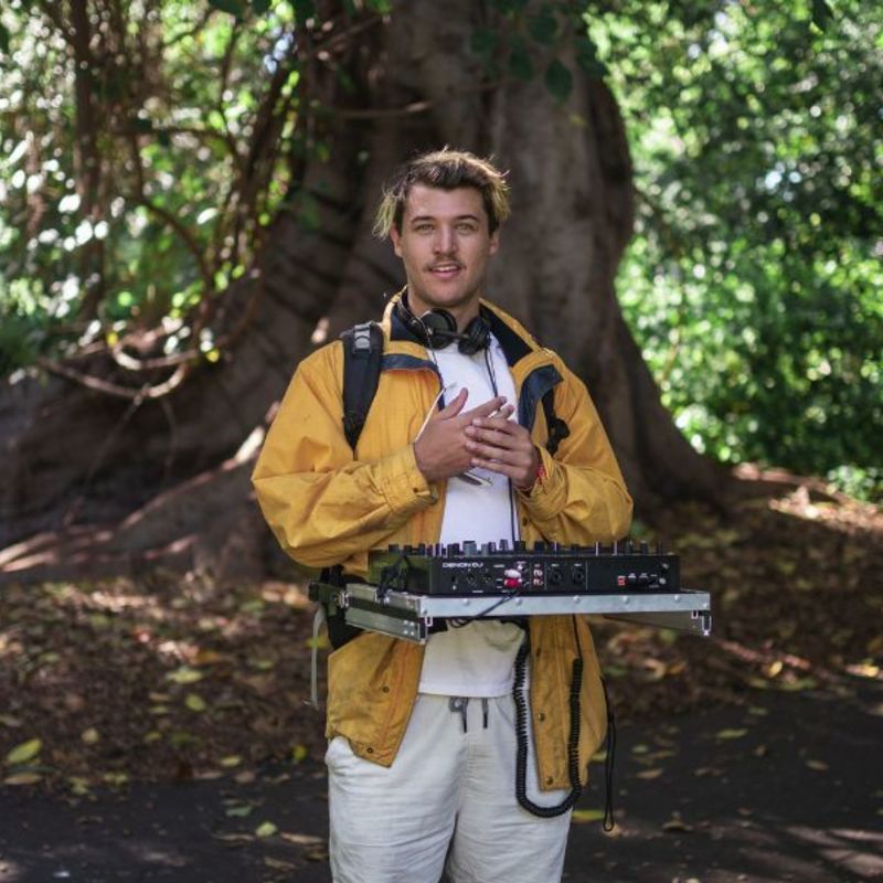 DJ Oscar Reed holding DJ decks in front of large tree
