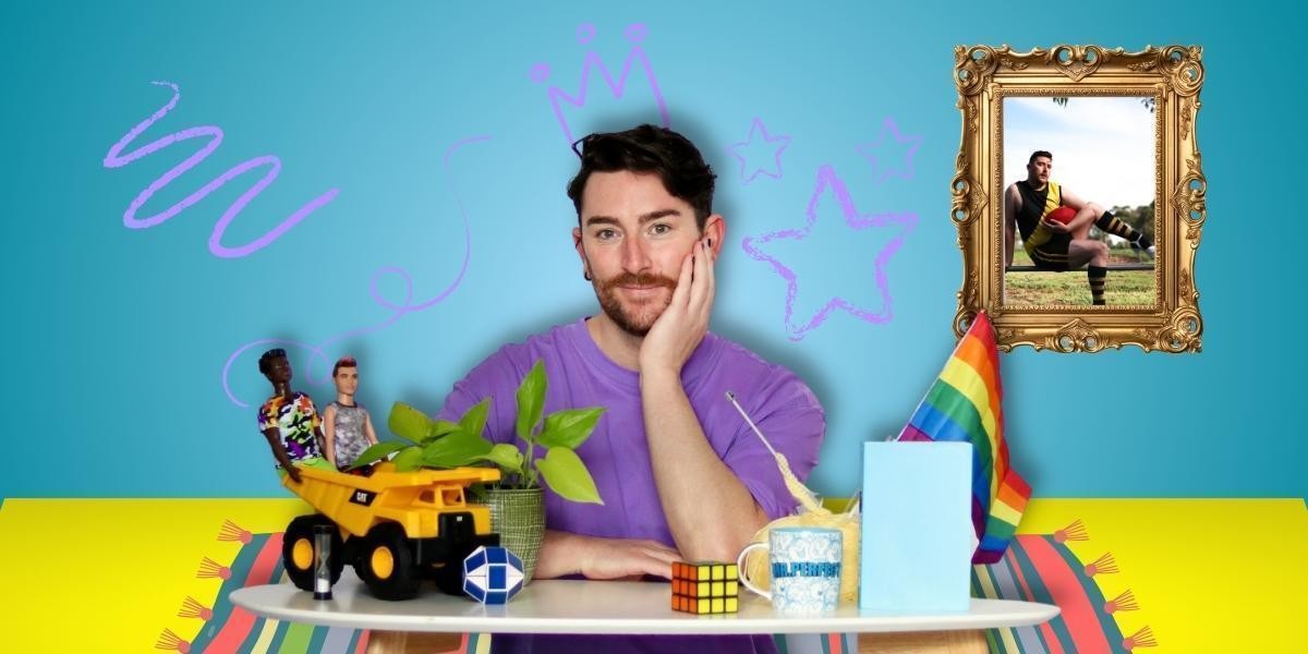 Photograph of a man in purple shirt sitting at a table of assorted toys and hobbies, with his hand on his cheek, smiling. With a cartoon background of a living room with crayon drawings on the wall and a framed picture beside his right