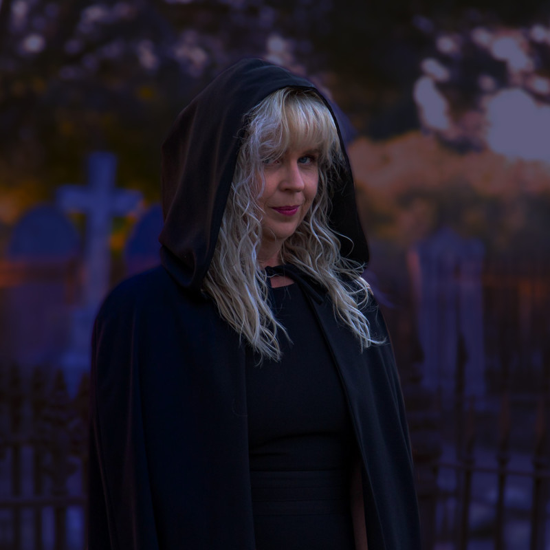 Woman in Cloak faces camera at night in front of graves