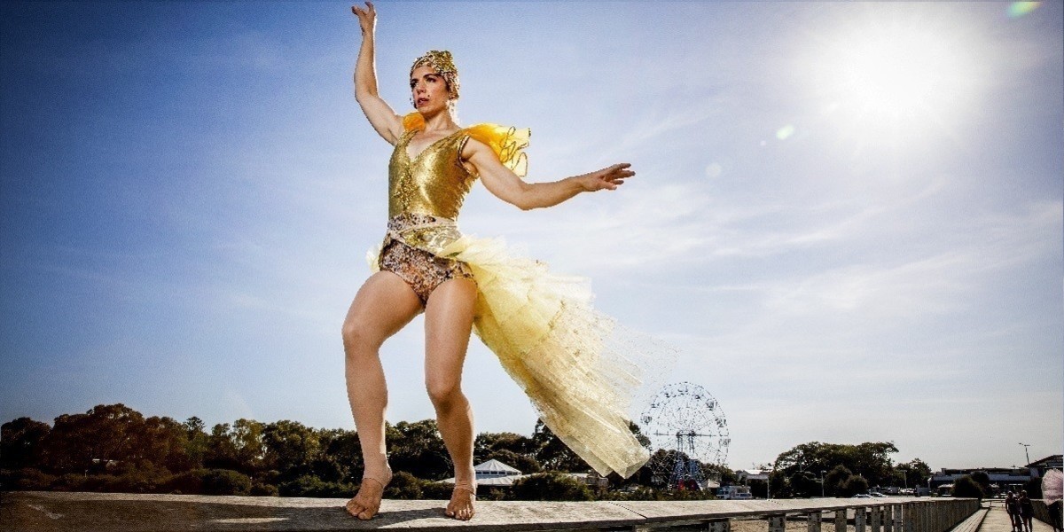 Jessica McCrindle is balancing on a bridge hand rail. She is dressed in a gold, sparkly outfit.